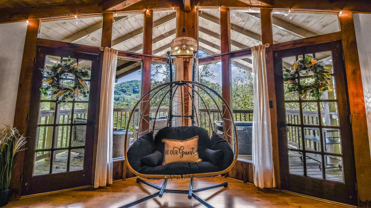 A cozy hanging chair sits by large glass doors, offering views of the outdoors and adorned with decorative wreaths. The inviting seating area suggests an easy transition from indoors to nature, ideal for relaxing after outdoor adventures.