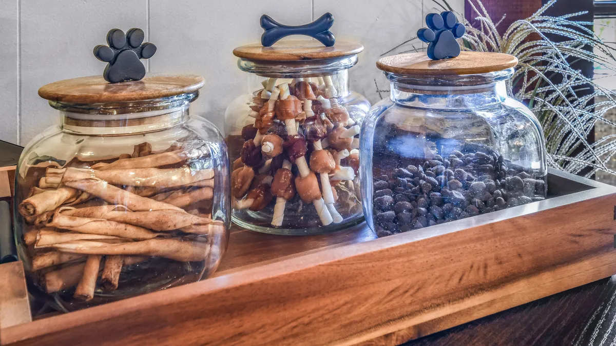 Three glass jars with wooden lids and playful paw-shaped handles are displayed on a wooden surface. The jars are clearly intended for pet treats or supplies, signaling the property's pet-friendly amenities.