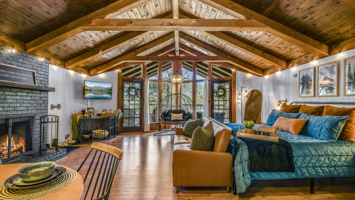A stylish living area featuring a glowing fireplace, a cozy hanging chair perfect for two, large windows framing the natural landscape, decorative pillows, and curated wall art. The ambiance is both intimate and welcoming.