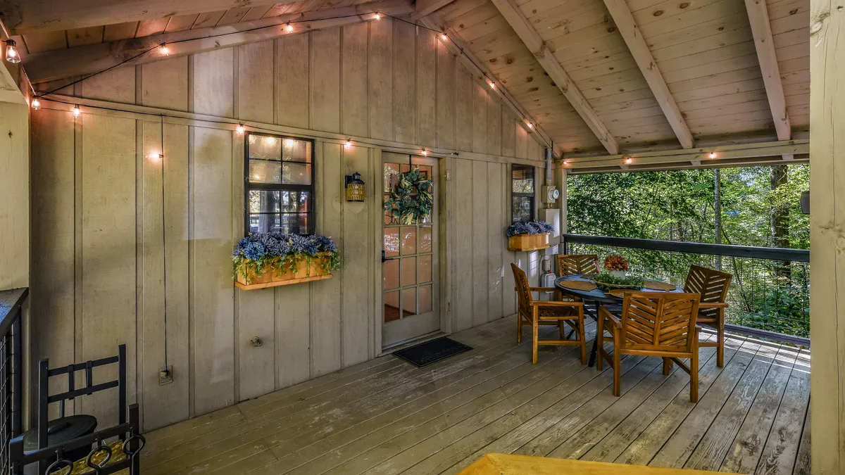 A wooden deck with comfortable outdoor seating, hanging plants, and a view through the doorway with glass panels. The space is ideal for sipping morning coffee or gathering with loved ones to recount the day’s adventures.