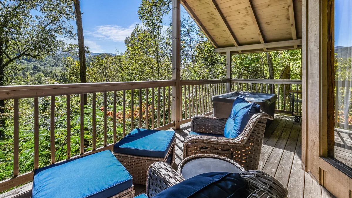 Comfortable wicker chairs with blue cushions are arranged on an outdoor deck overlooking a tranquil backdrop of trees. The mood is calm and inviting, creating an ideal spot for sipping morning coffee or evening stargazing.