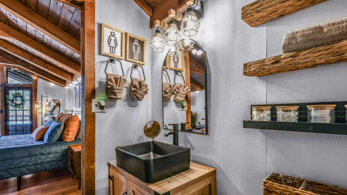 A chic bathroom vanity with a modern sink, wooden shelves neatly stocked with accessories, and a large, mirrored wall illuminated by soft lighting fixtures. The space feels both elegant and practical, ideal for grooming or winding down.