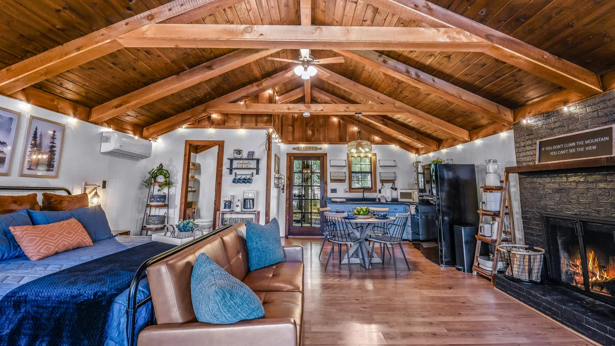 A warmly lit living area with a stone wood-burning fireplace as the centerpiece, flanked by a comfortable seating arrangement and adjacent to a dining space. The overall look blends modern comfort with rustic charm, ideal for gatherings and relaxing evenings.