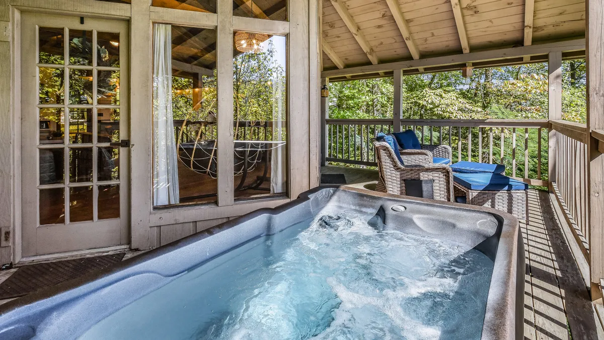 A serene interior lounge area featuring a hot tub and outdoor seating, visible through large glass doors. The setup offers a seamless transition from indoor comfort to outdoor vistas, ideal for unwinding after outdoor excursions.