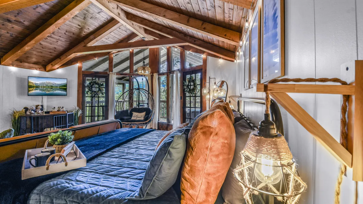 A serene bed with plush pillows and soft linens, adjacent to a hanging chair and large windows streaming in natural light. Decorative wall art and tranquil colors add a restful, welcoming feel to the sleeping area.