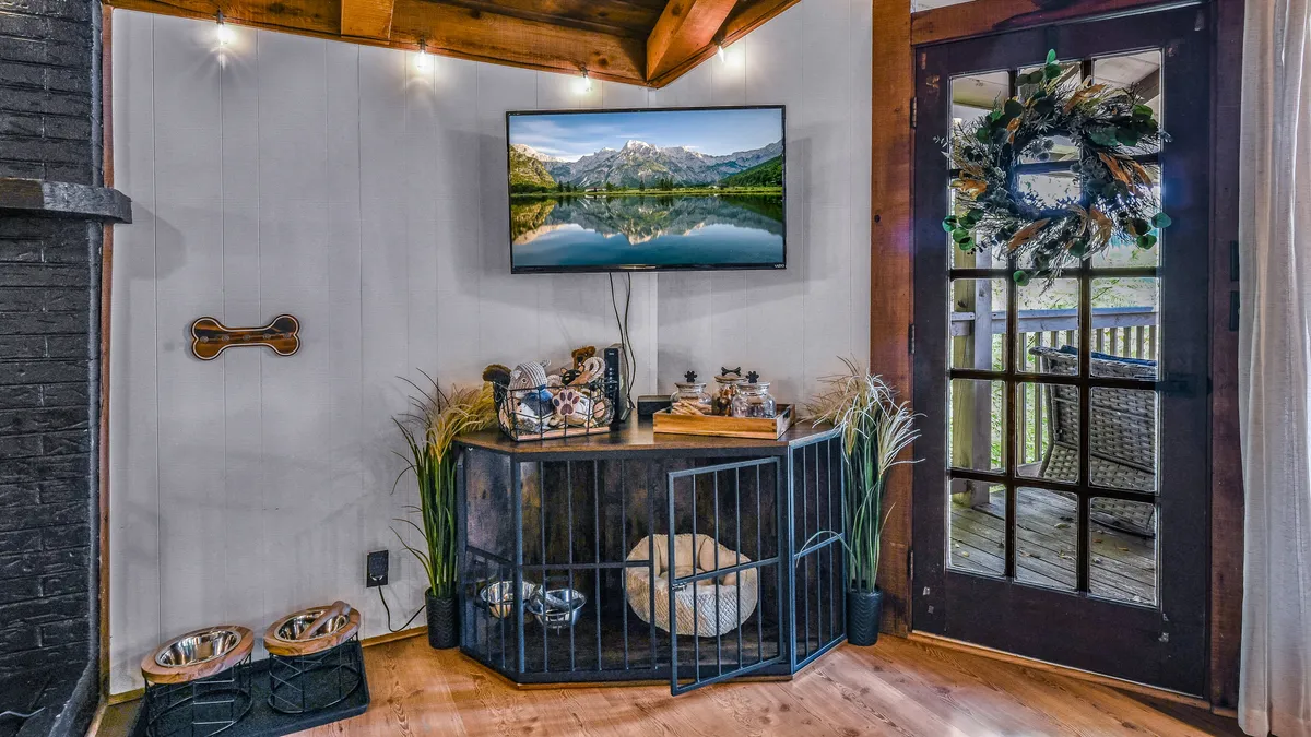A cozy living area with a television offering mountain views, a dedicated pet space with a decorative area for your furry companion, and a door leading outside. The scene highlights the integration of pet-friendly features within the home's welcoming ambiance.